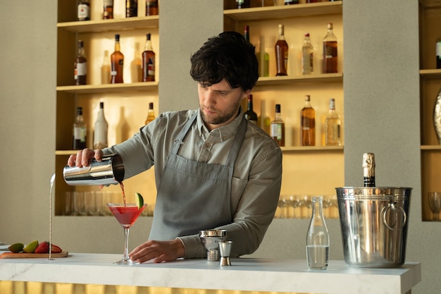 Barkeeper gießt kosmopolitischen Cocktail in Martini-Glas