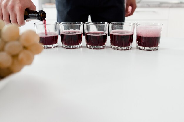 Barkeeper gießt Rotwein in Gläser auf weißem Tisch. Roter hausgemachter Wein in Gläsern.