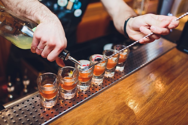 Barkeeper gießt starkes alkoholisches Getränk in kleine Gläser auf Bar, Schüsse.