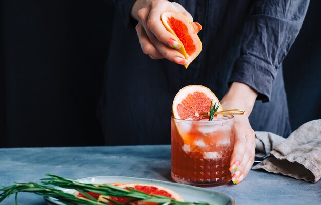 Barkeeper-Hand presst Saft aus frischer Grapefruit in Cocktail-Limonade mit Eis und Rosmarin.