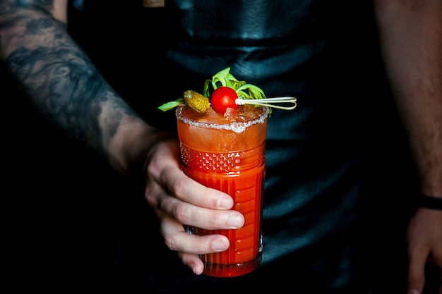 Barkeeper im weißen Hemd und in der dunklen Schürze, die eine Bloody Mary in das Cocktailglas auf der Bartheke gießt