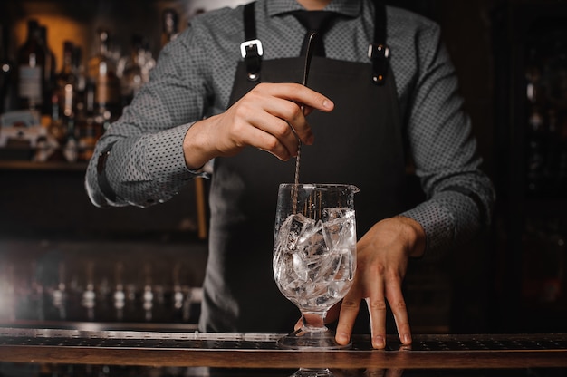 Barkeeper in der Schürze Eiswürfel mit Hilfe des Löffels rühren