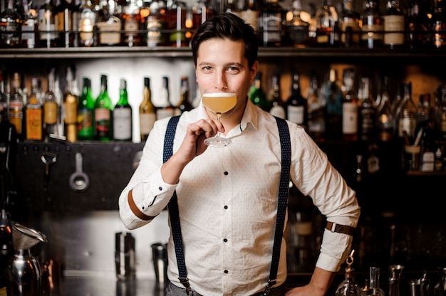 Barkeeper in weißem Hemd mit Cocktail an der Bar stehen