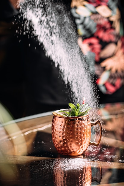 Barkeeper macht Cocktail in einem Kupferbecher mit Minze und Puderzucker