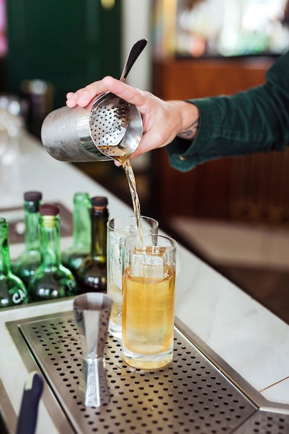 Barkeeper macht einen Cocktail an der Bar: Gießen Sie ein Getränk aus einem Shaker in ein Glas