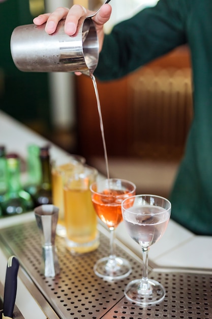 Barkeeper macht einen Cocktail an der Bar: Gießen Sie ein Getränk aus einem Shaker in ein Glas