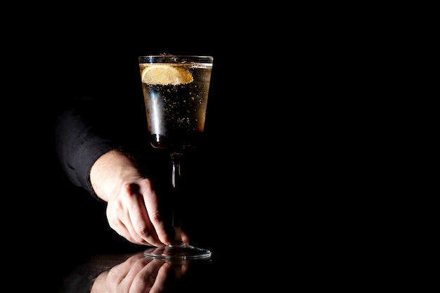 Barkeeper macht einen Cocktail mit Champagner in einem Glas auf schwarzem Hintergrund