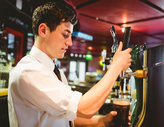 Barkeeper que sostiene el vidrio de cerveza debajo del golpecito del dispensador