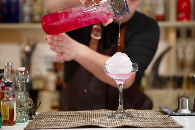 Barkeeper schenkt einen rosa Cocktail ein