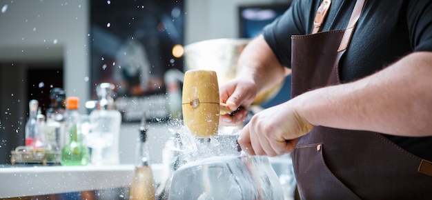 Barkeeper zerkleinert von Hand Eis mit Holzhammer und Metallmesser.