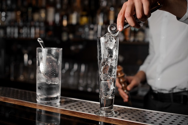 Barman, adicionando cubos de gelo em um copo vazio