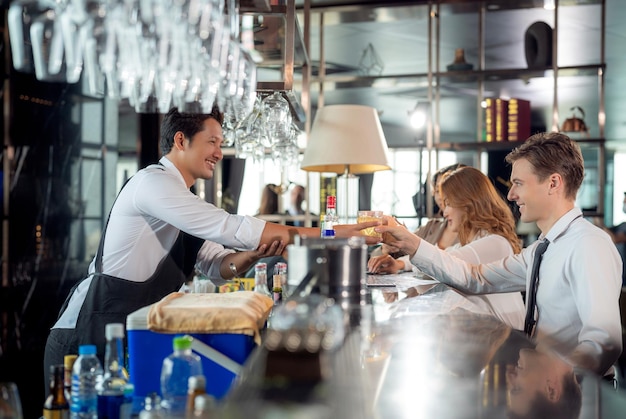 Barman asiático e seu cliente conversando em um bar e restaurante no telhado com balcão de bebidas