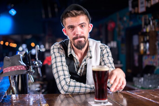 El barman barbudo decora brebajes coloridos mientras está de pie cerca de la barra del bar en la discoteca