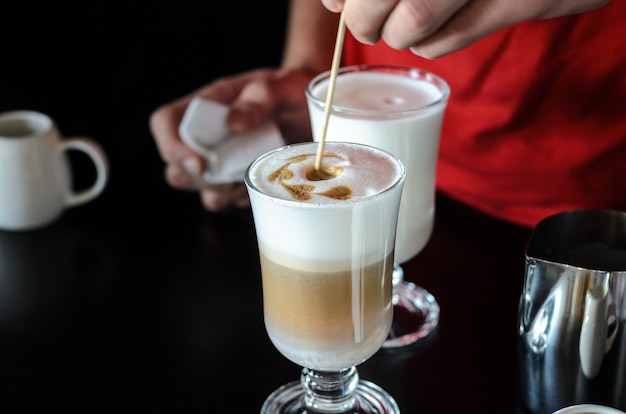 El barman Barista detrás del mostrador hace café con leche, sirve y evita