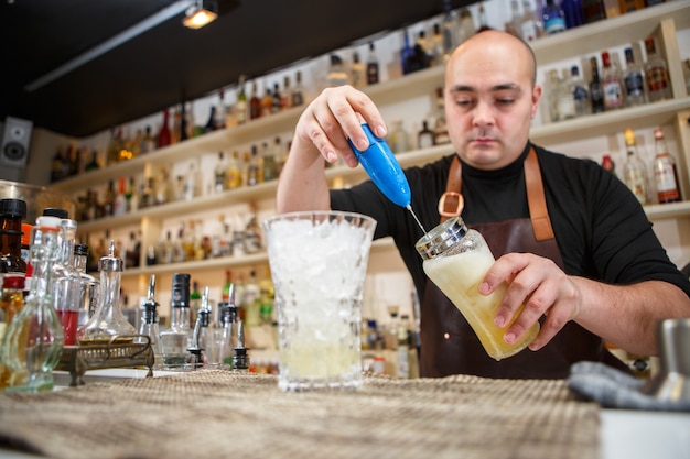 Barman con una batidora de mano para preparar bebidas en bar o pub