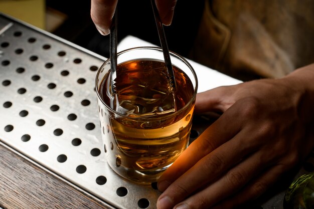 Barman, colocando um grande cubo de gelo para o coquetel de ouro no copo