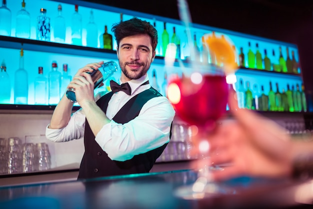 Barman considerável que prepara o cocktail no balcão de bar