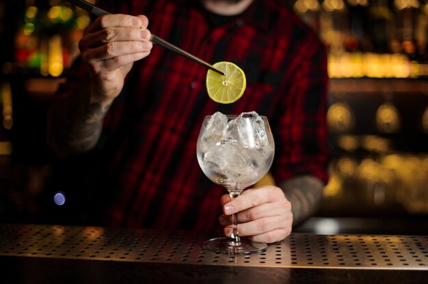 Barman decorar cóctel agrio fresco con una rodaja de limón y cubitos de hielo en la barra