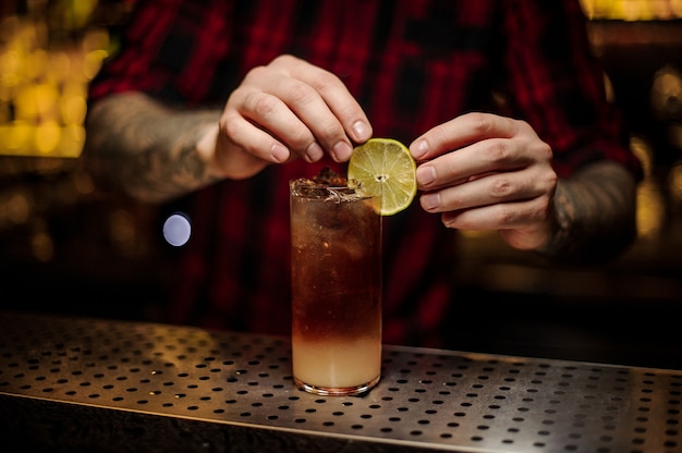 Barman decorar copa de cóctel con bebida alcohólica fresca con una rodaja de limón amarillo fresco