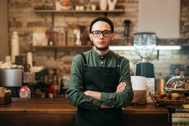 Barman en delantal negro de pie contra la barra de bar.