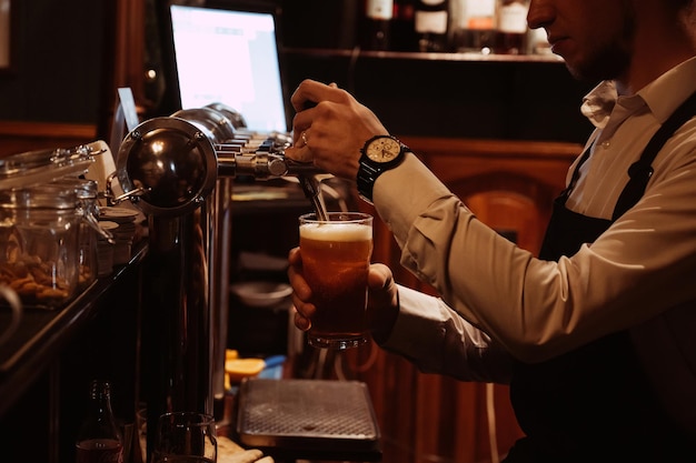 Barman derrama uma cerveja light com espuma em vidro de uma torneira em um pub atrás do bar