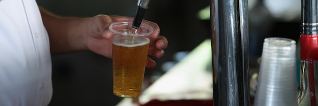 Barman derramando cerveja da máquina de torneira em vidro plástico grande