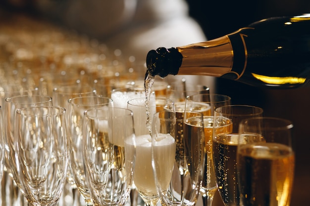 Barman, derramando champanhe ou vinho em taças de vinho em cima da mesa na cerimônia de casamento solene ao ar livre