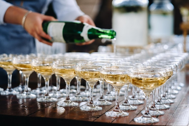 Barman derramando champanhe ou vinho em taças de vinho sobre a mesa na cerimônia de casamento solene ao ar livre