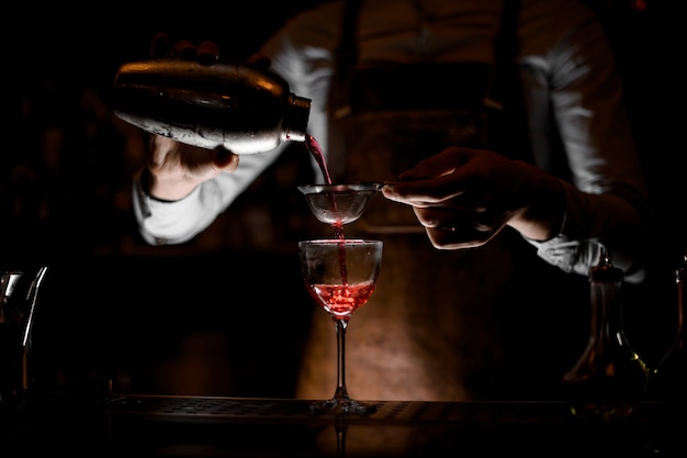 Barman, derramando coquetel com peneira em vidro