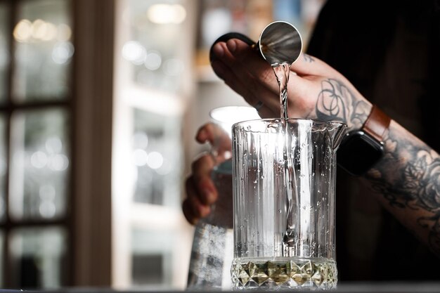 Barman derramando um álcool do copo de vidro medidor através do filtro para o coquetel no balcão do bar no fundo desfocado