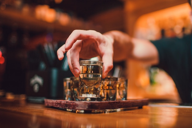 Foto barman está derramando tequila em vidro contra o fundo do bar.
