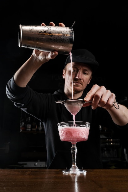 El barman está sirviendo un cóctel alcohólico Clover club rosa en el vaso El barman mezcla vermú seco de limón y clara de huevo y ginebra para preparar el cóctel Clover club