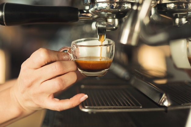 Barman experiente fazendo café expresso em uma máquina de café moderna. Close-up da mão feminina preparando uma bebida estimulante. Conceito de fabricação de café para pequenas empresas e profissionais