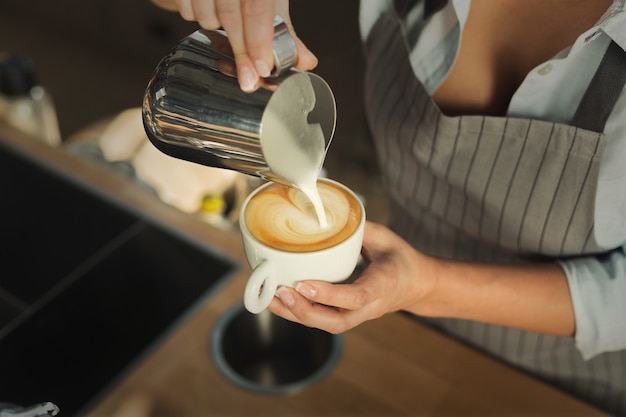 Barman fazendo cappuccino. Close da mão feminina, derramando espuma de leite quente no café expresso. Latte art, pequenas empresas e conceito de fabricação de café profissional