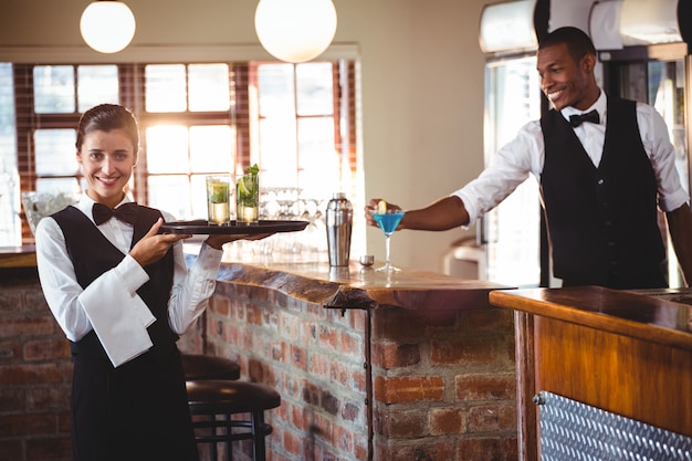 Barman feminino segurando uma bandeja com dois copo de cocktail