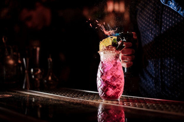 Barman haciendo un dulce y fresco cóctel de verano de mojito de fresa con una nota de humo sobre el fondo oscuro