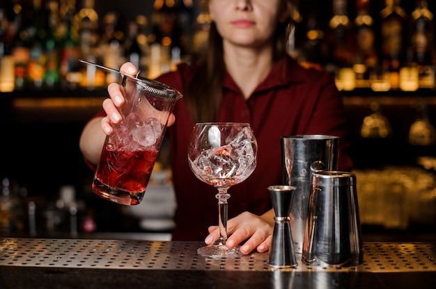 Barman hembra vertiendo dulce bebida alcohólica roja en un vaso