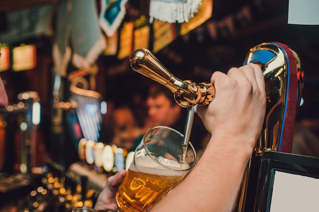 Barman manos vertiendo una cerveza en un vaso.