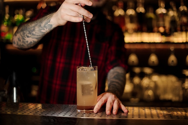 Barman mexendo um coquetel de limonada com a colher no copo no balcão do bar