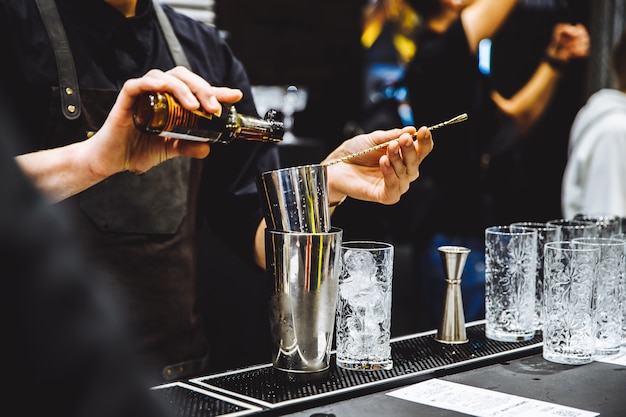 Barman no trabalho despejando álcool em copos e preparando coquetéis com detalhes. Foto de alta qualidade