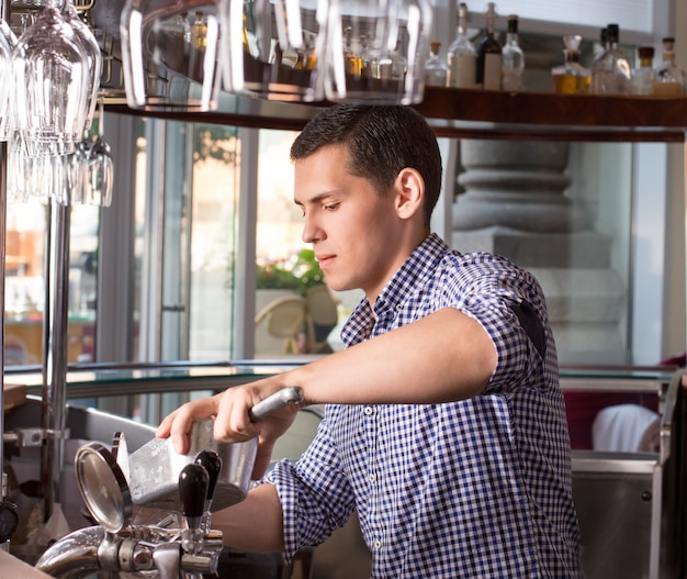 Barman novo considerável atrás do balcão da barra que guarda a colher de aço do gelo.