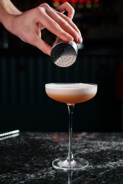 Barman polvilha o coquetel com canela preparando bebidas em um bar