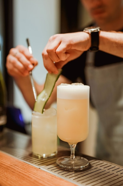 Barman preparando gin tônica com pepino no fundo, coquetel pina colada em primeiro plano. Foto com profundidade de campo rasa. Imagem vertical do estilo de vida.
