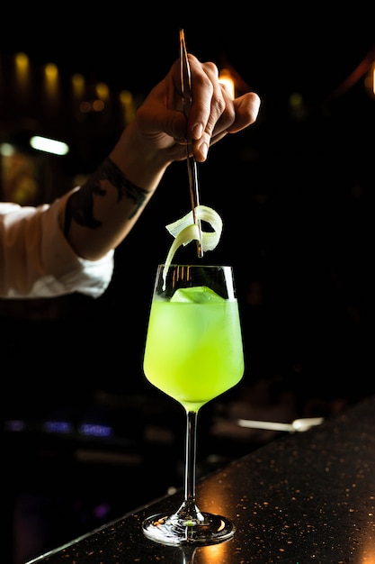 Barman preparando um coquetel, adicionando guarnição de aipo em um copo de vinho com uma bebida gelada de cor verde