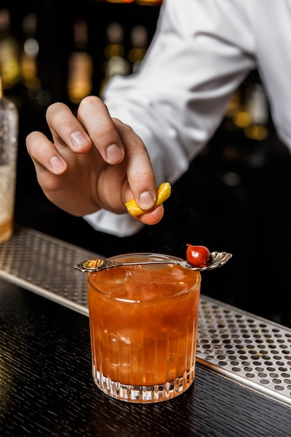 Barman preparando um coquetel no bar, espremendo uma casca de limão sobre uma bebida em um copo de pedras