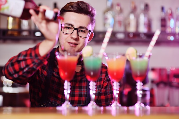 Barman profissional prepara e mistura cocktails derramando xarope vermelho de uma garrafa de um bar em uma boate