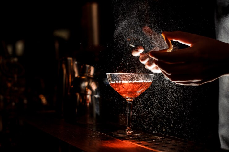 Barman pulveriza uma casca de laranja em copo de coquetel