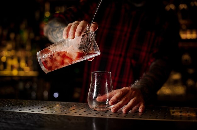 Barman servindo coquetel vermelho agridoce fresco e saboroso em um copo de coquetel vazio no bar