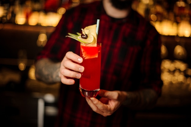 Barman servindo um coquetel Hurricane Punch decorado com limão e abacaxi seco no balcão do bar