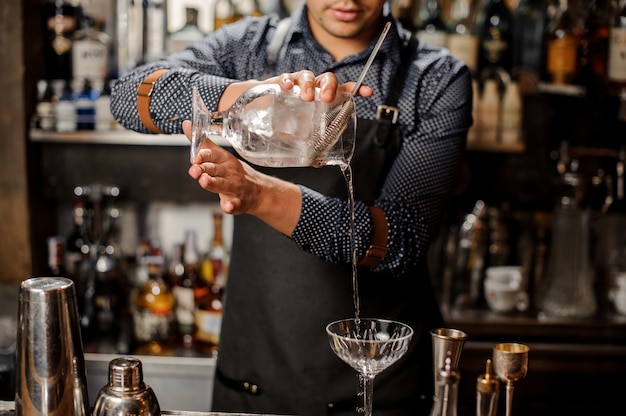 Barman vertiendo bebida alcohólica fría en una copa de cóctel